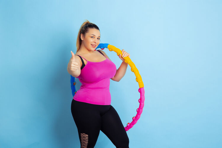 手年轻的白人大号女模特在蓝色背景下的训练运动概念 人类情感 表达 健康的生活方式 身体积极 平等摆出篮球姿势 竖起大拇指健康运动员饮食