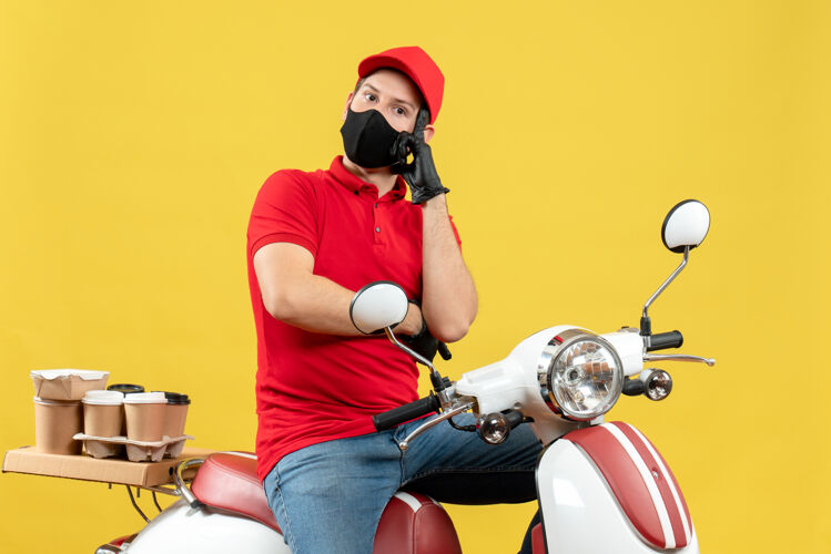 命令俯视图：体贴的年轻人穿着红色上衣 戴着帽子手套 戴着医用面罩 坐在黄色墙上的滑板车上传递命令摩托车医疗车辆