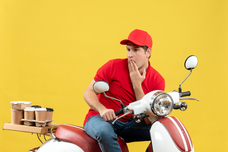 年轻人俯视图：穿着红色上衣 戴着帽子的体贴的年轻人在黄色的墙上传递命令衬衫身体摩托车