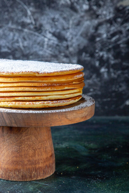 水平正面图薄薄的蛋糕层和糖粉放在圆木板深色的表面上蛋糕前面木头
