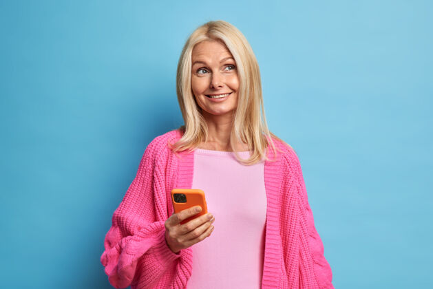 女人面容姣好 忧郁愉快的金发女人穿着暖和的针织粉色套头衫 用手机上网交流女士女性梦幻