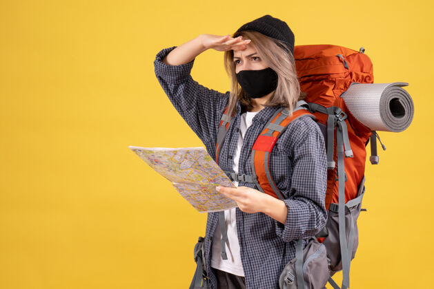 成人正面图酷酷的旅行女孩带着黑色面具和背包拿着地图在看什么帽子背包肖像