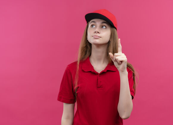 复制令人印象深刻的年轻送货女孩在红色制服抬起手指在孤立的粉红色空间与复制空间女孩提高年轻