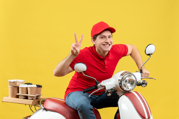 年轻人俯视图：身着红色上衣 头戴帽子 面带微笑的年轻人在黄色的墙上传递命令 做出胜利的手势交付健身车辆