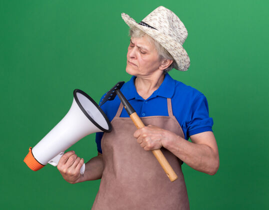 园艺笨手笨脚的上了年纪的女园丁戴着园艺帽 拿着耙子 看着果岭上的扩音器老人帽子喇叭