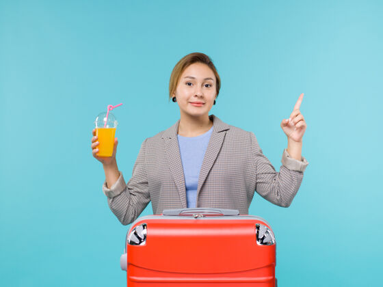 微笑正面图：度假中的女性拿着她的红色袋子拿着新鲜果汁坐在蓝色的办公桌上度假飞机旅行海上旅行前面红色蓝色