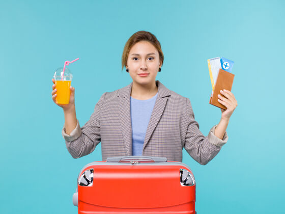 人正面图：度假中的女性手拿新鲜果汁和蓝色背景的机票海上度假飞机旅行女人前面假期