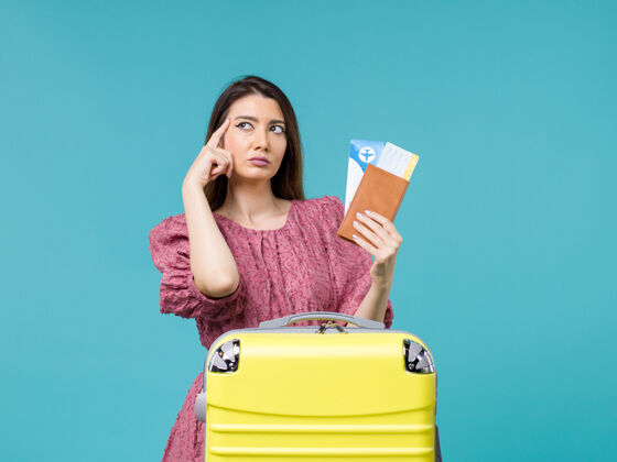 风景正面图度假中的女性拿着她的钱包和机票在蓝色背景下旅行度假旅行的女性夏日大海前面假期微笑