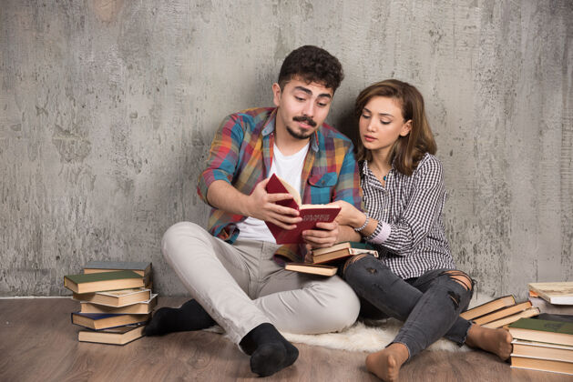 举行可爱的夫妇坐在地板上读一本有趣的书家庭生活阅读房子