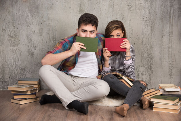 肖像一对可爱的情侣躲在书后面看着前面男人阅读夫妇