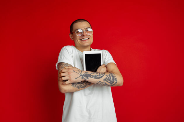 白种人红色工作室墙上的高加索年轻人肖像 具有丰富的情感和表现力年轻人人平板电脑