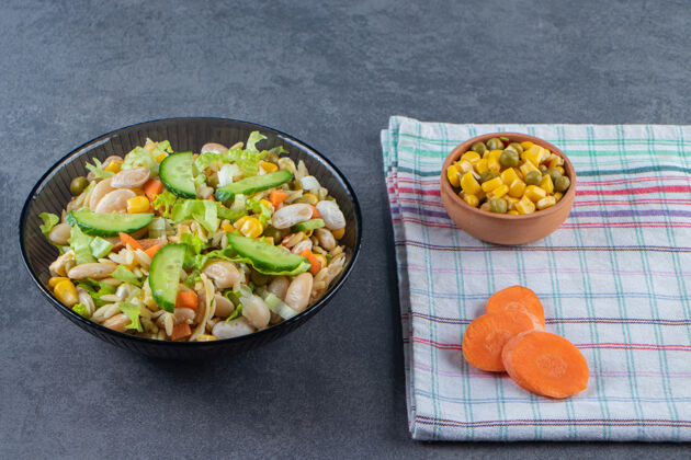 毛巾两碗蔬菜沙拉和胡萝卜片放在茶巾上 放在大理石表面胡萝卜盘子蔬菜