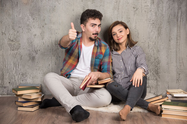 模特一对年轻夫妇拿着书坐在地板上竖起大拇指坐着地板女孩