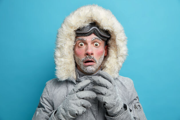 惊喜冻僵的男性探险家红着脸 满脸霜冻 瞪着眼睛 对极低的温度感到非常震惊 穿着暖和的夹克和手套 在暴风雪寒冷的天气里走在户外夹克寒冷男