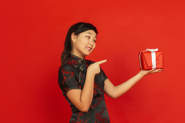 情感指着礼物2020年中国新年快乐红色背景上孤立的亚洲少女肖像穿着传统服装的女模特看起来很快乐庆祝 节日 情感复制空间旗袍美丽手