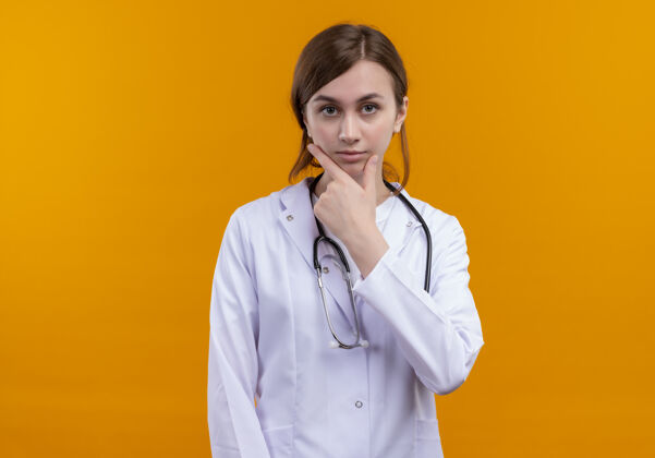 医学一位面容严肃的年轻女医生 穿着医用长袍 手放在下巴上的听诊器 放在一个孤立的橙色空间里 还有复印空间橙色太空手