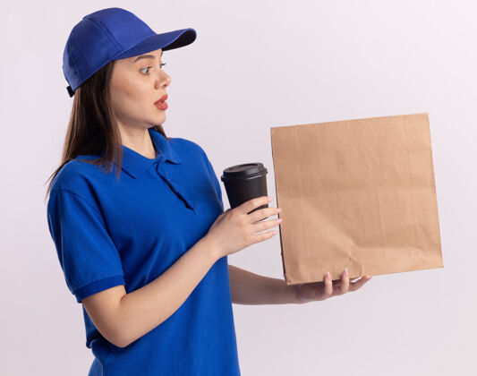 着急穿着制服的焦急漂亮的女送货员拿着纸杯 看着白色的纸包装纸包装女人