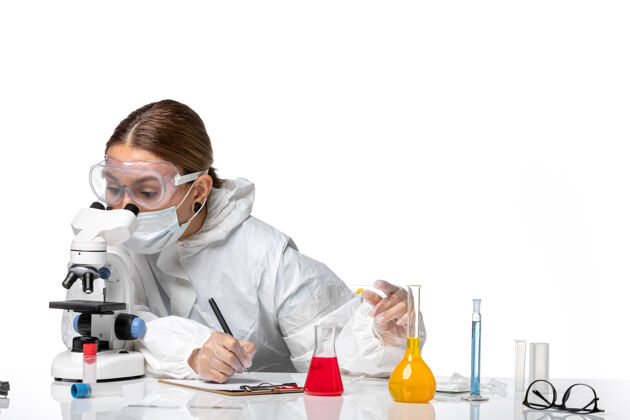书写前视图：穿着防护服 戴着口罩的女医生在浅白色背景上写笔记医学病毒-健康大流行病毒医疗防护套装