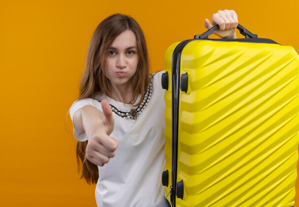女孩自信的年轻旅行家女孩举起手提箱 在孤立的橙色空间竖起大拇指信心展示手提箱