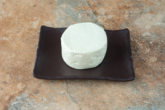 大理石一块白色的圆奶酪放在大理石桌上的深色盘子里深色盘子食物