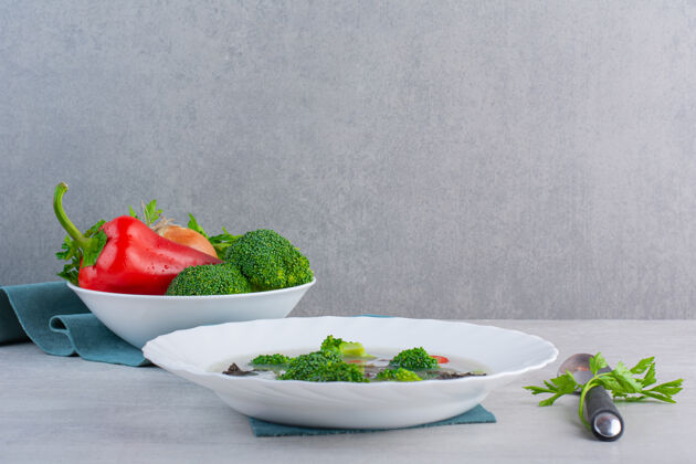 营养白碗新鲜蔬菜汤和有机蔬菜放在石头表面晚餐洋葱混合