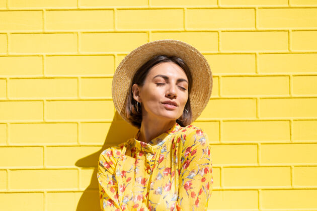 肖像黄砖墙上戴着黄色夏装和帽子的女人沉着而积极 享受着阳光明媚的夏日城市脸旅游