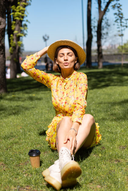 人穿着黄色夏装戴着帽子坐在公园草地上的女人的户外肖像成人肖像旅游