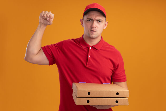 感觉自信的年轻送货员穿着制服 戴着帽子拿着披萨盒 在橙色的墙上显示出强烈的手势手势帽子展示