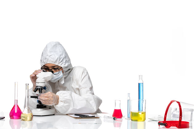 大流行前视图穿着特殊防护服的女化学家在白色背景上用显微镜检查样本化学冠状病毒大流行人套装医学