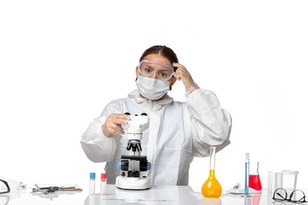 男人前视图女医生穿着特制的工作服 戴着口罩 用显微镜观察一种浅白色背景病毒-冠状病毒大流行医生医学实验室外套