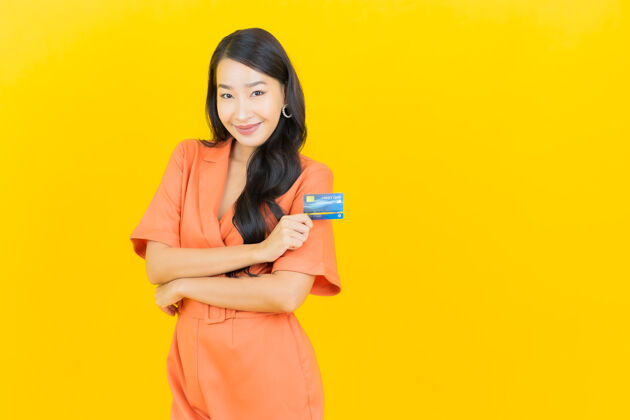 橙色连身衣肖像美丽的亚洲年轻女子微笑信用卡上的黄色显示人手机