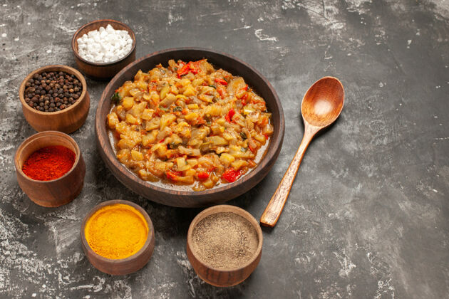 食物顶视图烤茄子沙拉在碗和不同的香料在碗木勺叶在黑暗的表面不同的料理餐具