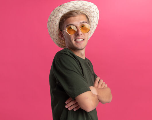人带着微笑的年轻帅哥 穿着绿色衬衫 戴着眼镜 戴着帽子 双手交叉 隔离在粉红色的墙上 留着复印空间衣服手市民