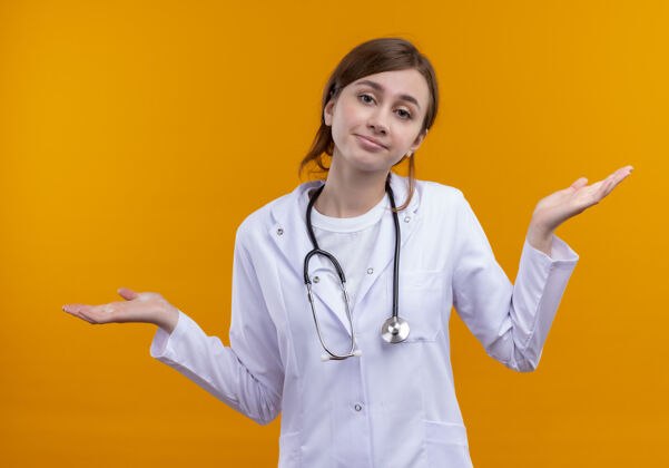 表演困惑的年轻女医生穿着医用长袍和听诊器 在孤立的橙色空间里空手而归困惑空虚穿
