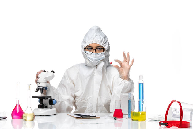 大流行前视图穿着特殊防护服的女化学家在白色背景化学冠状病毒大流行上用显微镜检查样本白人专业病毒