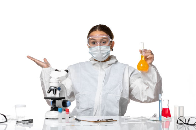 专业人员正面图：女医生 穿着特制的工作服 戴着口罩 白色桌子上放着黄色溶液的瓶子 里面有冠状病毒烧瓶药品面罩