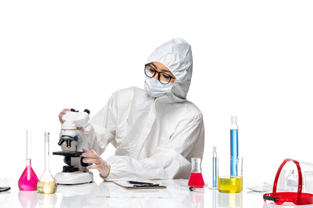 药品前视图穿着特殊防护服的女化学家在白色背景上用显微镜检查样本化学冠状病毒-健康病毒显微镜化学白色