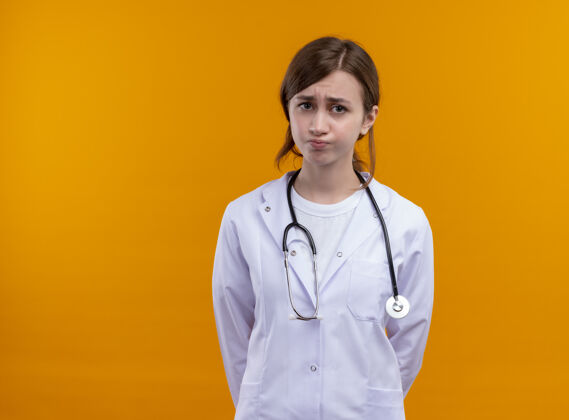 女焦虑的年轻女医生穿着医用长袍和听诊器站在孤立的橙色空间与复印空间穿长袍橙色