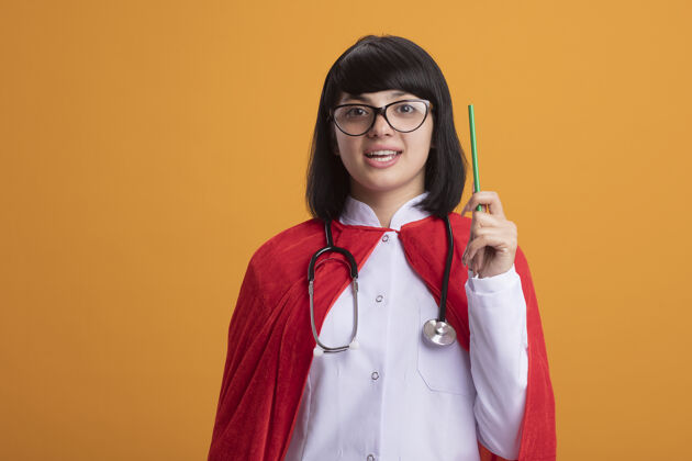 眼镜令人印象深刻的年轻超级英雄女孩戴听诊器与医疗袍和斗篷与眼镜提高铅笔超级英雄铅笔穿