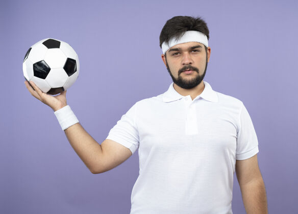 足球自信的年轻人戴着头带和腕带 在一旁举着球球运动持有