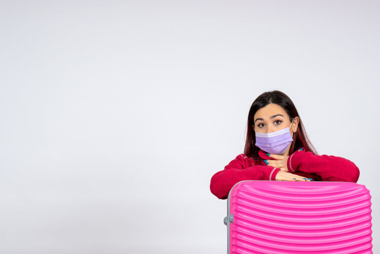 女人正面图：年轻女性 带着粉色袋子 戴着无菌口罩 在白色墙壁上度假 是一位流行性感冒病毒的旅行女性大流行游客小