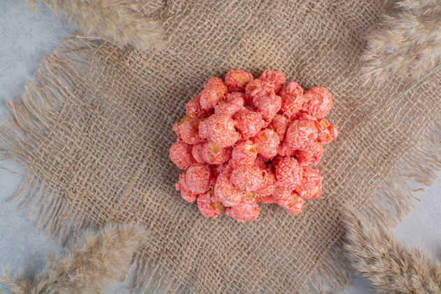 成分一小堆红色爆米花糖放在一块布上 周围是大理石表面的干草外套釉料糖果