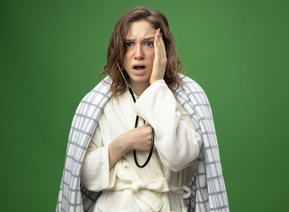 包被吓坏了的年轻病女孩穿着格子布包裹的白色长袍 用听诊器把手放在绿色的脸颊上 听着自己的心跳疾病绿色格子