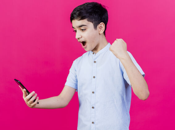 年轻人快乐的小男孩抱着手机看着粉红色的墙上做着“是”的手势表情抱着是的
