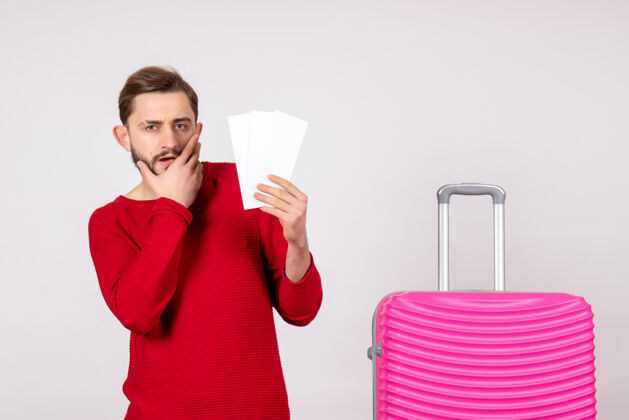 情感正面图年轻男子手拿粉红包 手持飞机票上白墙远航航班旅游度假情感照航班旅游飞机