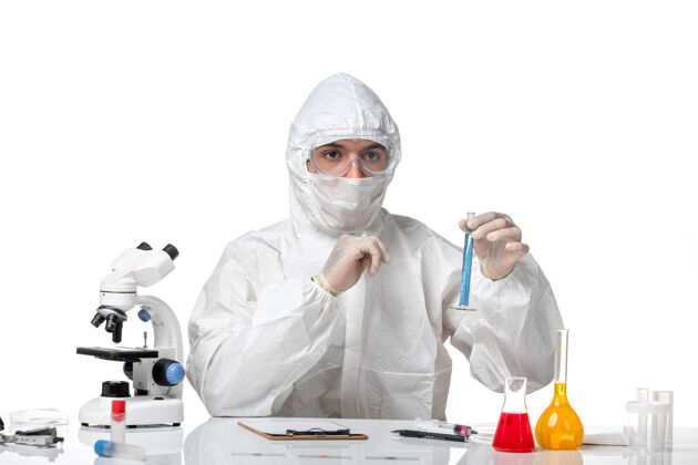 化学正面图：男医生穿着防护服 戴着口罩 白色桌子上放着一个装有蓝色溶液的瓶子医生外套烧瓶