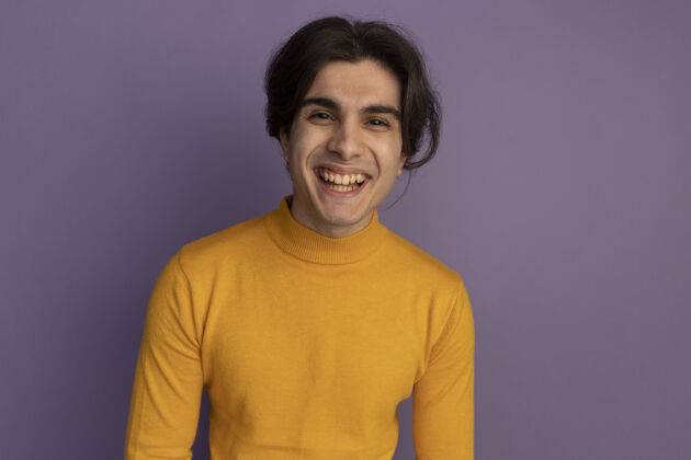 帅气带着微笑的年轻帅哥穿着黄色高领毛衣隔离在紫色的墙上 留着复制空间穿微笑小伙子