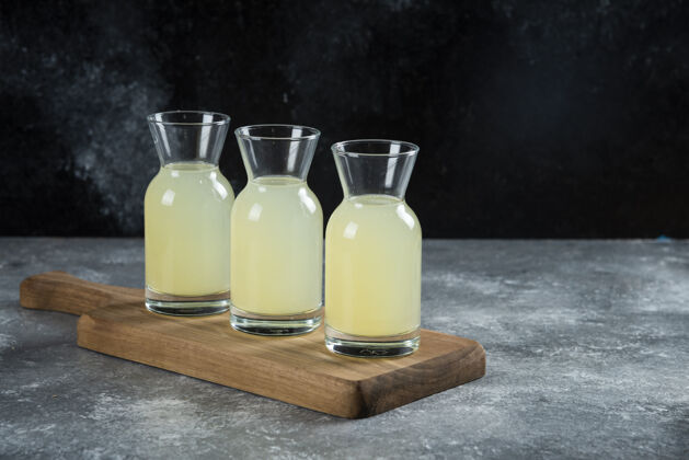 酸味三个装着新鲜柠檬汁的玻璃罐放在木板上果汁凉的木头