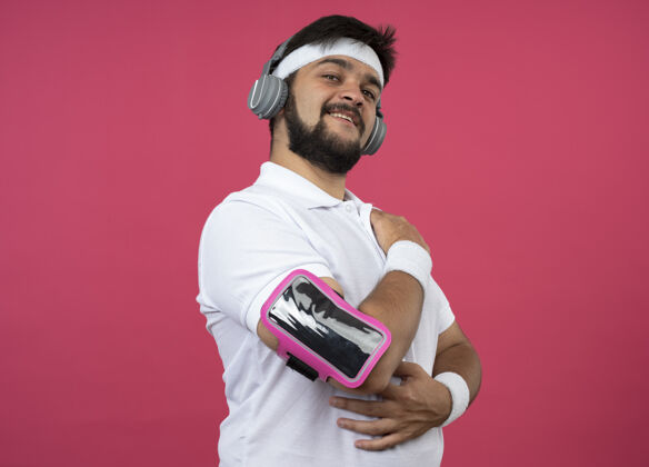 乐队喜欢运动的年轻人戴着头带和腕带 带着耳机和电话臂带 隔离在粉红色的墙上手臂头带电话