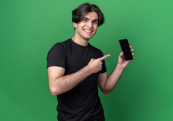 电话面带微笑的年轻帅哥身穿黑色t恤 手拿手机指着绿色墙上的隔离墙抱帅男人